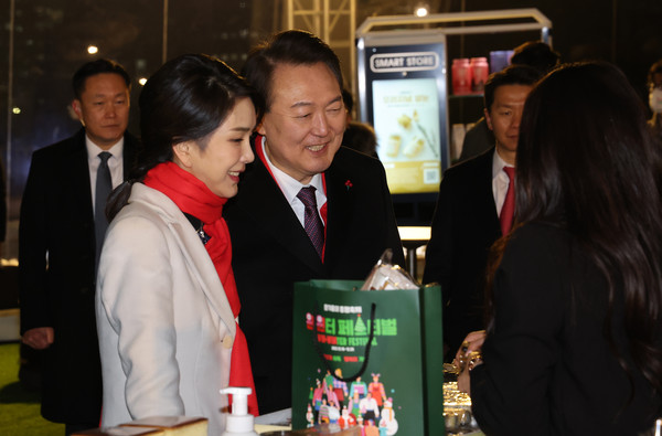 윤석열 대통령과 김건희 여사가 지난 16일 오후 서울 종로구 열린송현광장에서 열린 윈·윈터 페스티벌 개막식에서 에어돔 부스를 방문, 물건을 구입하고 있다.(사진 연합뉴스 제공)