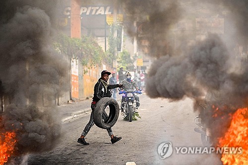아이티의  수도 포르토프랭스에서 시위자가 타이어를  불태우며 아리엘 앙리 총리의 사임을 요구하고 있다 (사진, AFP=연합뉴스)